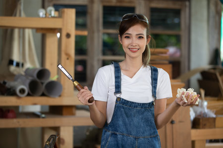 Young woman is training to be a carpenter in workshop. Carpenter working with equipment on wooden table. woman works in a carpentry shop.の写真素材