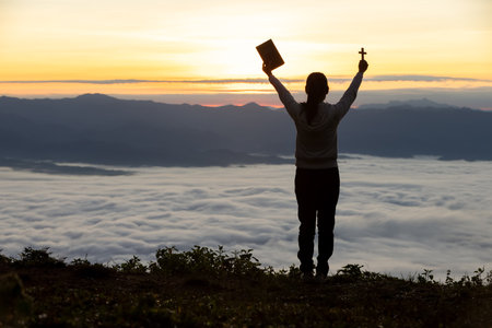 Silhouette of a woman praying on a mountain at sunrise. Young woman praying to God.の写真素材