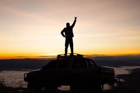 Silhouette of a man on the roof of a car on a mountain at sunrise.の写真素材