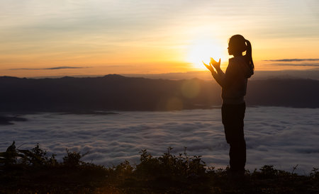 Silhouette of a woman praying on a mountain at sunrise. Young woman praying to God.の写真素材