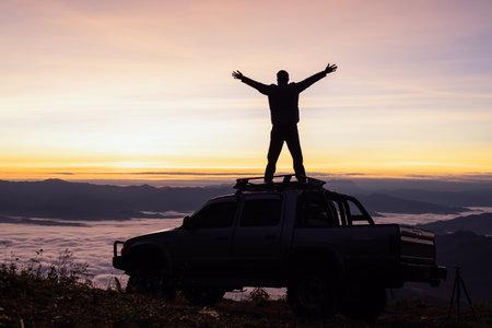 Silhouette of a man on the roof of a car on a mountain at sunrise.の写真素材