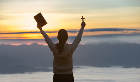 Silhouette of woman praying while holding Bible and cross, Pray in the Morning , Woman praying with hands together on the Sunrise background.の写真素材