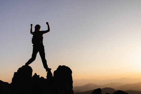 Silhouette of  A person standing on top of the mountain Travel and adventure. Mountain hiking. Mountains during sunrise. Success and goal achievement. People success.の写真素材