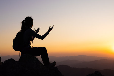 Silhouette of a woman is praying on the mountain. Praying hands with faith in religion and belief in...