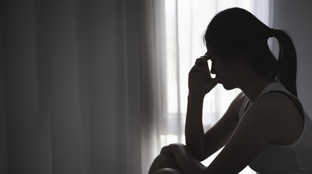 Teenager girl with depression sitting alone on the sofa in the dark room.