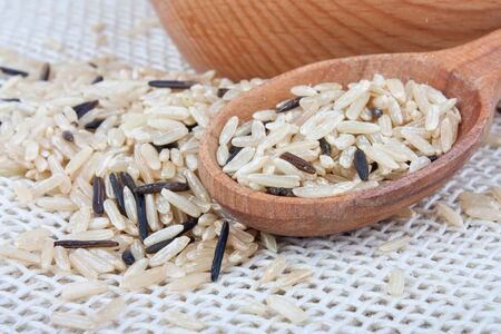 Raw wild rice in wooden bowl and spoon on burlap, food ingredient photoの写真素材