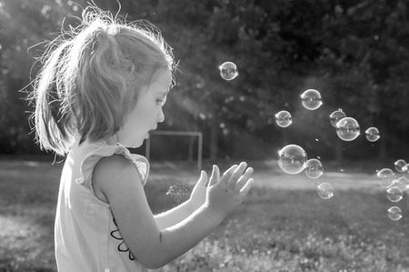 Cute little girl blowing soap bubbles on nature backgroundの写真素材