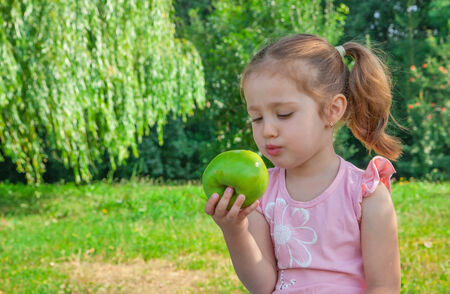 Cute little girl eating green apple on nature backgroundの写真素材