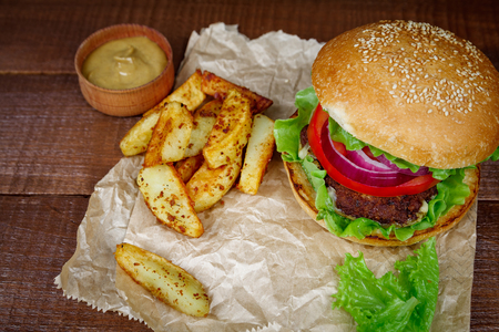 Tasty grilled beef burger with lettuce and potatoes on paper and wooden background. Big hamburger for lunch. Food photo.の写真素材