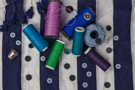 Sewing tools and sewing kit with color thread coils and buttons on clothing textured background