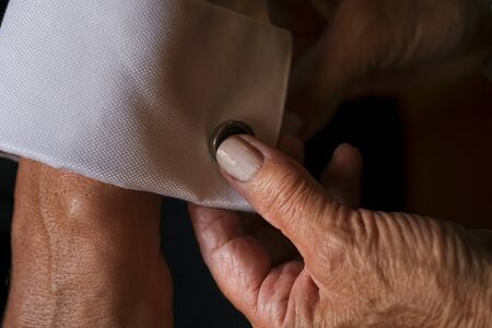 mother of the groom fastening cuffs and cufflinks before the weddingの写真素材