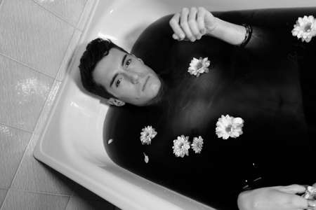 beautiful boy with white shirt posing in bathtub portrait while smokingの写真素材