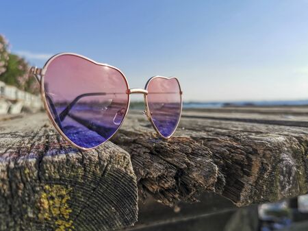 heart-shaped sunglasses on wooden pier with sun and reflection of lake gardaの写真素材