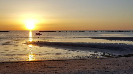 sunrise on the beach of the mediterranean sea in riccione rimini with sun reflected sand and wavesの写真素材