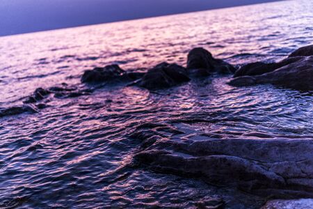 beautiful sunrise on lake garda went up with rocks and waves, with reflection of the colors of the sunの写真素材