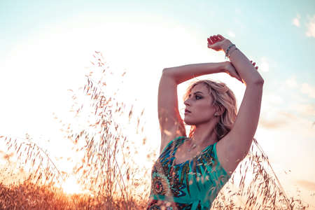 beautiful blonde girl with red dress and white hat at sunset in wheat field with sunglasses. High quality photoの写真素材