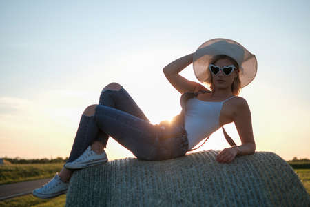 beautiful blonde girl in wheat field with white shirt and country jacket at sunset. High quality photoの写真素材