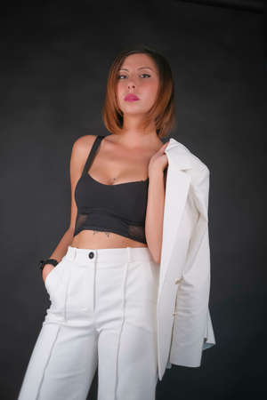 beautiful brunette girl with short hair wearing glasses and white shirt and pants posing on stool. High quality photoの写真素材