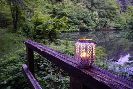 metal lantern with lit candle on wooden ruler on mountain lake. High quality photoの写真素材
