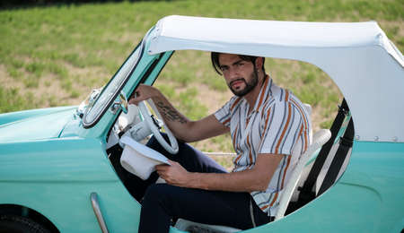 portrait of beautiful dark-haired italian model man with light eyes with beard in an old italian tiffany car. High quality photoの写真素材
