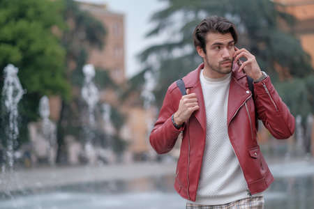 beautiful guy with red leather jacket and backpack in the center of reggio emilia. High quality photoの写真素材