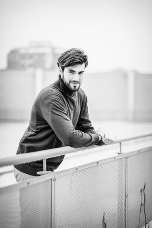 handsome Italian dark-haired guy leaning against metal railing with red sweater. High quality photoの写真素材