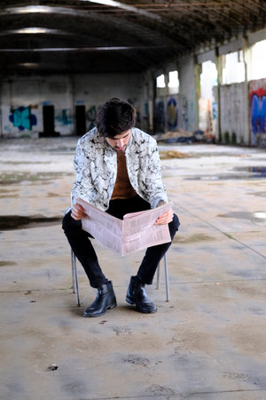 beautiful Italian dark-haired boy reads the newspaper in the abandoned factory. High quality photoの写真素材