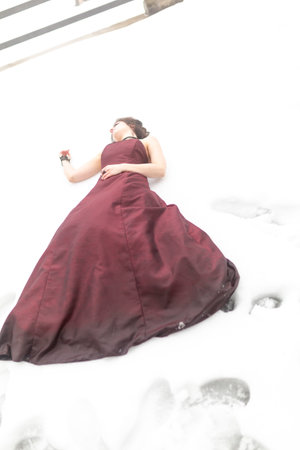 beautiful brunette vampire girl with blood red dress lying dead in the snow. High quality photoの写真素材