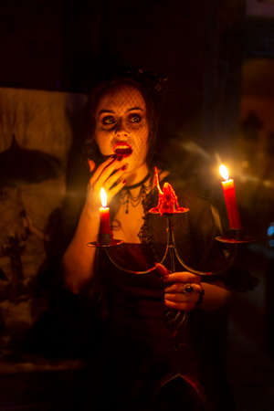 beautiful brunette vampire girl with bloody teeth walks around a castle with a candle in her hand. High quality photoの写真素材