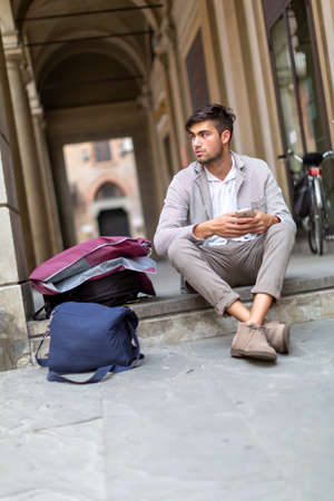 handsome Italian dark-haired guy sitting on city steps while using smartphone. High quality photoの写真素材