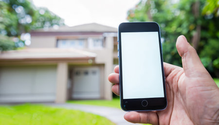Hand holding smart phone with blank screen in front of new house.の素材