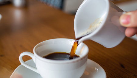 Coffee pouring into a white cup on a wooden table.の素材