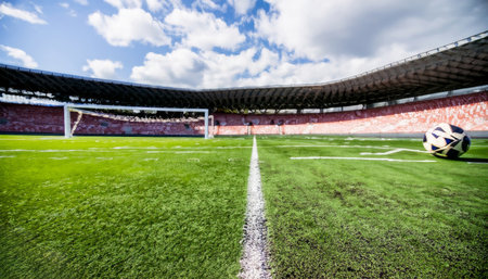 Soccer ball on the green grass of football stadium under blue skyの素材