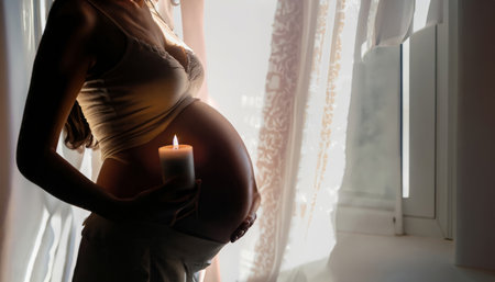 Pregnant woman holding a candle in her hands and looking out the windowの素材