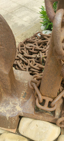 The image presents a closeup view of a rusty chain lying upon a rough concrete surface, showing its...