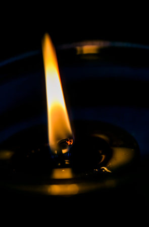 This is a detailed closeup of a beautifully lit candle illuminating the darkness around it, creating...