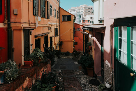 A narrow street in a colorful Italian town, with tall buildings painted in warm hues and lush potted...