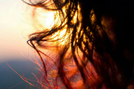 A silhouetted profile of a woman with long hair, gazing towards a vibrant, golden sunset sky.