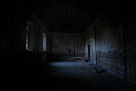 Inside a dimly lit room, there is a single source of light emanating softly from the ceiling above, creating a contrast with the surrounding darknessの写真素材