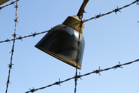 Close-up of a lamp amidst barbed wire at Dachau, an emblematic image of the camp's oppressive environment and historical significance. High quality photoの写真素材