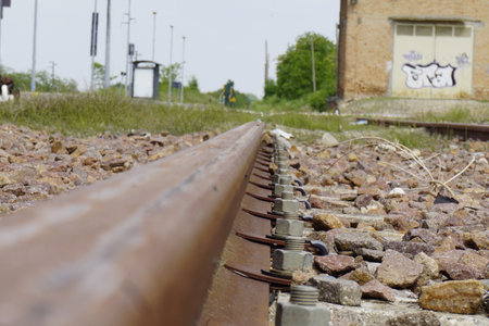 A close-up, low-angle shot of a rusty railroad track, highlighting the texture and perspective, with blurred background details. Keywords:. High quality photoの写真素材
