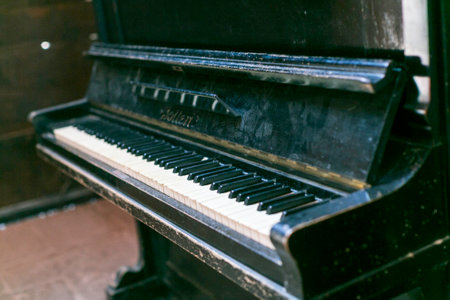 A vintage, upright piano with a distressed, black finish, showcasing its age and character, set against a simple backdrop. High quality photoの写真素材