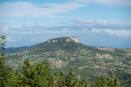 A distant view of the Pietra di Bismantova, a flat-topped mountain, stands prominently over rolling hills under a cloudy sky, showcasing a scenic landscape. Reggio Emilia. High quality photoの写真素材