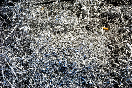 A close-up, detailed view of a large pile of shiny, curled metal swarf and sharp shavings, remnants...