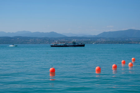 A peaceful view along the shore of Lake Garda, Italy, featuring calm blue water lapping against a rocky edge. High quality photoの写真素材