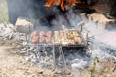 A sturdy portable metal grill sits on the ground, filled with glowing hot coals and scattered ash, ready for outdoor cooking or recently used. High quality photoの写真素材