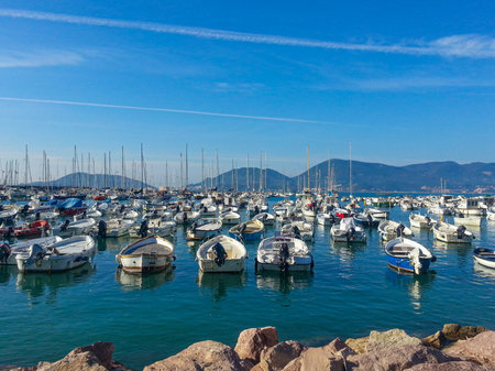 Numerous leisure boats and sailing yachts are moored in the calm waters of Lerici's picturesque port, with the town and hills visible in the background under a blue sky. High quality photoの写真素材