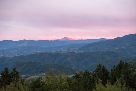 A breathtaking mountain landscape at twilight, featuring a distant peak bathed in warm pink and orange light under a soft, colorful sky. High quality photoの写真素材