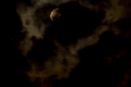 A vibrant, glowing full moon is partially veiled by dark and illuminated golden clouds, creating a...