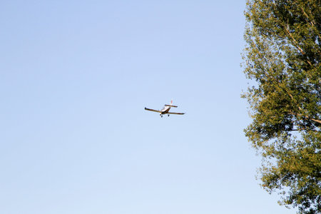 A light single-engine propeller airplane flying high in a clear blue sky, framed by the green...